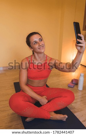 Portrait of young gorgeous woman using a smartphone after a yoga exercise. She is sitting on floor and taking a photo with her phone.