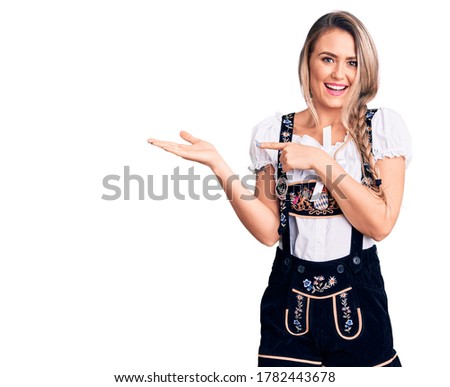 Young beautiful blonde woman wearing oktoberfest dress amazed and smiling to the camera while presenting with hand and pointing with finger. 