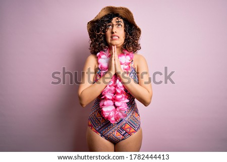 Young beautiful arab woman on vacation wearing swimsuit and hawaiian lei flowers begging and praying with hands together with hope expression on face very emotional and worried. Begging.