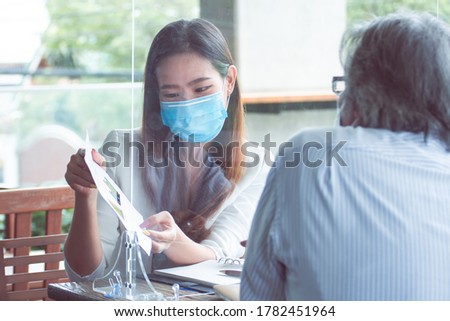 Asian woman and boss wearing masks, keeping social distancing and working together