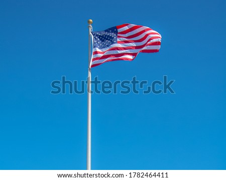 Flag of the United States of America waving in the wind on a clear blue sky background.