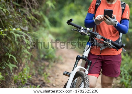 Cyclist use smartphone when riding mountain bike on forest trail
