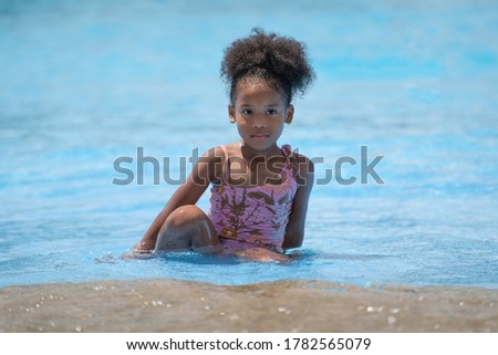 African black girl sitting and playing water in swimming pool at amusement park.  Concept kid are expressing pure joy and excitement