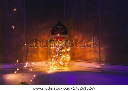 A glass jar with light bulbs and a red Christmas ball. Blue light. The reflection of light on the ceramic tile. Home decoration for the holiday. The concept of New year or Christmas