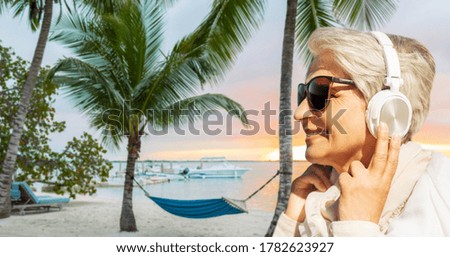 technology, old people and leisure concept - senior woman in headphones and sunglasses listening to music over tropical beach background in french polynesia