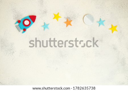 Close up. White-gray texture. Above is a space-themed pattern. Blue rocket and multicolored stars, moon. Sweets. Copy space.