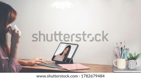 Photo of young asian woman using tablet making video call with her friend while sitting in living room at home.