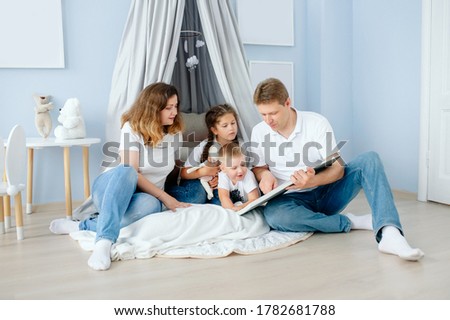 family reading a book mom dad daughter and son sitting on the floor in the children's room