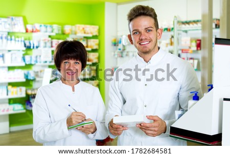 Portrait cheerful pharmacist and pharmacy technician posing in pharmacy. Focus on the man
