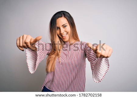 Young beautiful blonde woman with blue eyes wearing stiped t-shirt over white background approving doing positive gesture with hand, thumbs up smiling and happy for success. Winner gesture.
