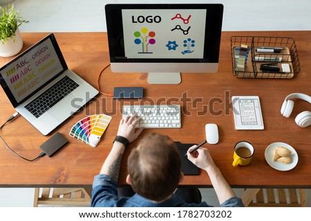 Above view of logo designer sitting at desk and editing icon design using drawing pad