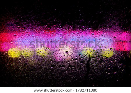 Rain on a window with colourful neon lights behind at night time