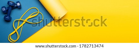top view of blue fitness mat with dumbbells and resistance band on yellow background, panoramic shot Royalty-Free Stock Photo #1782713474
