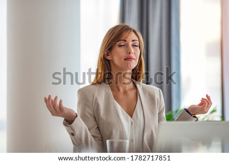 Businesswoman relaxing doing yoga at office. Carefree businesswoman relaxing doing yoga exercises at office. Woman in office meditating. Businesswoman meditating in her office