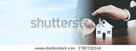 Insurer protecting a house with his hands; panoramic banner