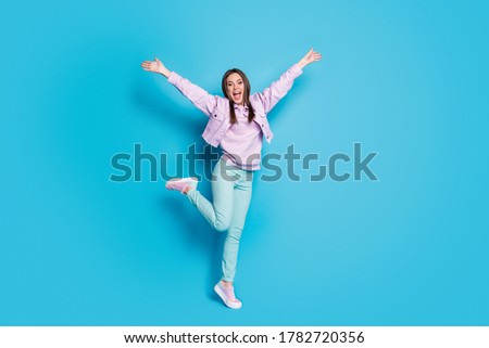 Full length photo of crazy funny lady raise hands leg up students party good mood meet friends wait hugs wear casual denim violet jacket pullover pants shoes isolated blue color background