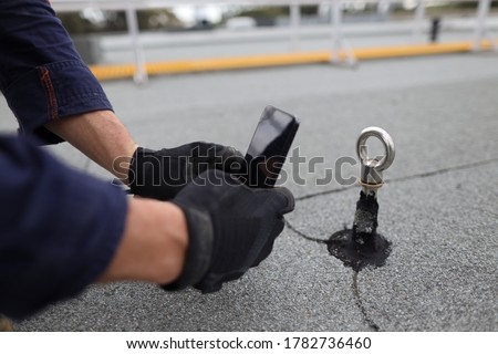 Inspector auditor technician using his phone photographing fall arrest, fall restraint roof anchor point
horizontal safety line while conducting yearly safety inspection prior used     