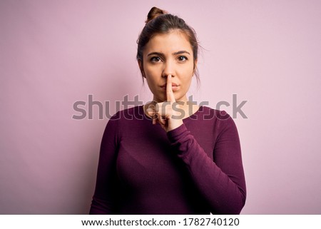 Beautiful young woman wearing casual bun hairstyle over pink isolated background asking to be quiet with finger on lips. Silence and secret concept.