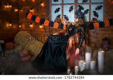 Halloween young beautiful witch is sitting in a chair and holding an apple in her hand. Candles are burning on the floor. Magic picture