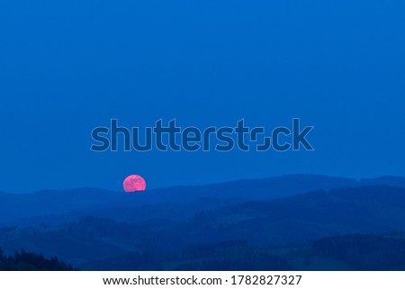 Red moon rising from a mountain area after sunset.