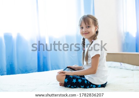 Portrait of cutie little girl playing on digital tablet while sitting at home in living room.