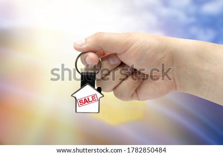 A man's hand holds a keychain in the form of a house with the inscription Sale on the background of the flag of Alberta. Property and real estate sale concept.