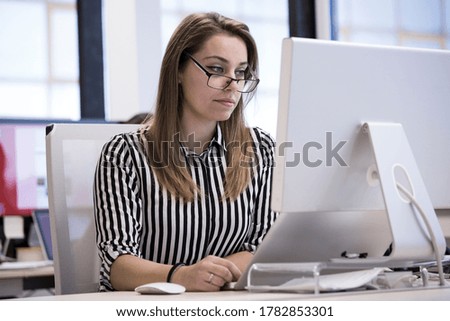blonde manager with glasses and striped shirt works in the office sitting in front of her workplace