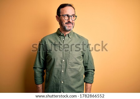 Middle age hoary man wearing casual green shirt and glasses over isolated yellow background smiling looking to the side and staring away thinking.