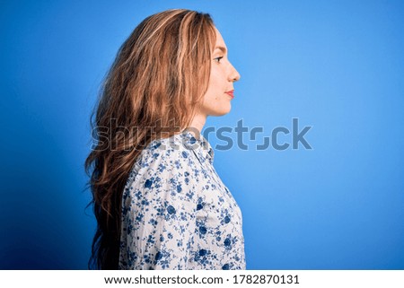 Young beautiful blonde woman wearing casual shirt standing over blue background looking to side, relax profile pose with natural face with confident smile.