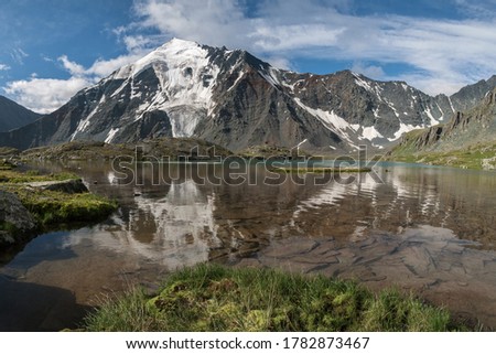 Glacier on a mountain peak. The mystical face of a ghost is reflected in the lake. Altai, Russia.