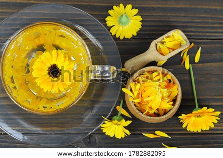 Calendula tea in transparent cup on wooden background
