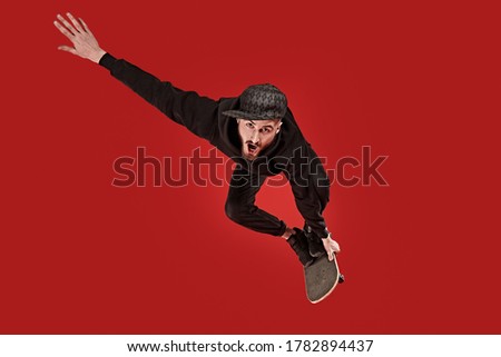 Cool young man rides and does tricks on a skateboard. Active lifestyle. Studio portrait on a red background.