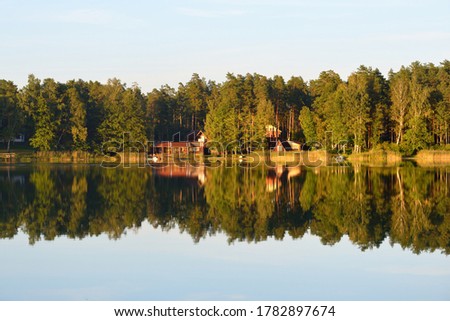 Country houses, evergreen trees and a river at sunset, Latvia. Symmetry reflections on the water. Autumn landscape, idyllic rural scene. Environmental conservation, eco tourism theme