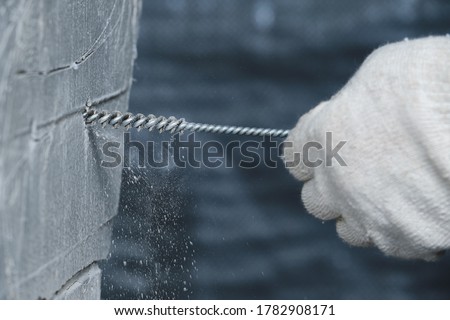 Cleaning of small holes drilled in a concrete wall for chemical anchors from crumbs and dust. Work process. Hand in a glove. Metal brush
