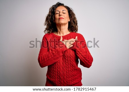 Middle age brunette woman wearing casual sweater standing over isolated white background smiling with hands on chest with closed eyes and grateful gesture on face. Health concept.