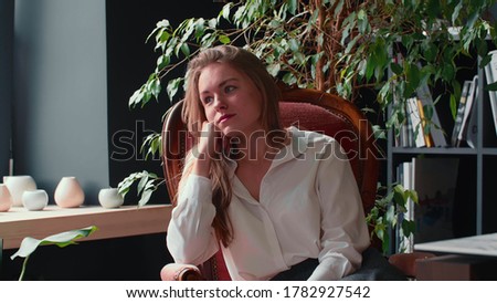 Lifestyle portrait of beautiful young blonde 20s business woman looking at camera smiling surprised on loft cafe chair.