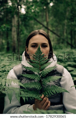 portrait of young woman with leaf of a fern in forest