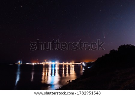 Comet C/2020 NEOWISE at night star sky and sea with city lights