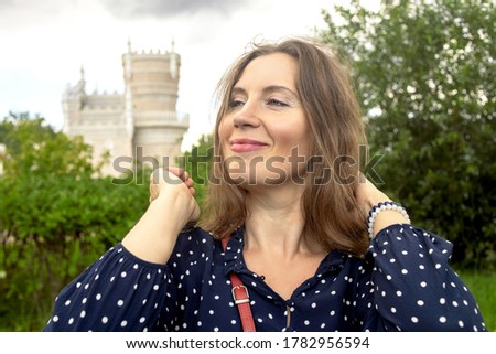 Outdoor portrait of attractive middle-aged successful mature smiling female brunette in blue polka dot dress on park natural background. Selective soft focus. Text copy space