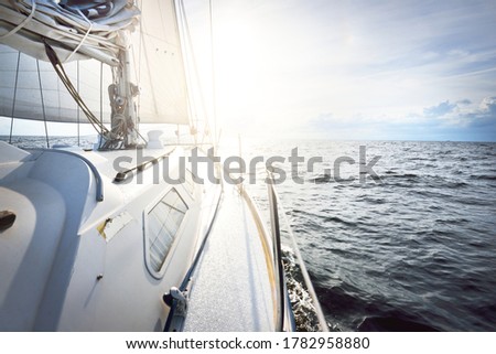 White yacht sailing in an open sea at sunset. Close-up view from the deck to the bow and sails. Dramatic sky with colorful clouds after the storm. waves and water splashes. Sport and recreation theme Royalty-Free Stock Photo #1782958880