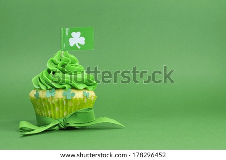 Happy St Patrick's Day green cupcakes with shamrock flags and leprechaun hat against a green background