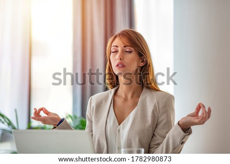 Peaceful concentrated businesswoman sit at office desk meditating at workplace, calm focused woman worker with mudra hands practice yoga manage emotions. Stress free concept