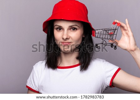 Closeup portrait of businesswoman showing mini shopping cart, online shop, ecommerce concept. e-commerce and shopping concept. Woman wearing white t-shirt holding mini shopping cart on hand.
