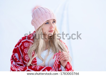 Portrait of a cute woman against the snow in a pink hat and red plaid posing for the camera.