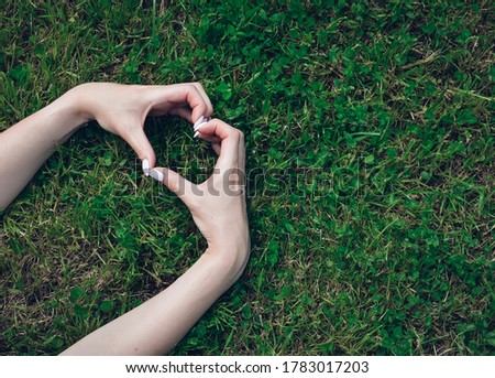 Female hands making a heart sign with fingers, on grass background. Love concept for valentines day.