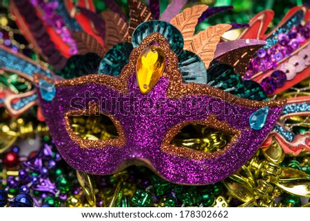 Close up view of purple sequined Mardi Gras mask with colorful beads out of focus in the background