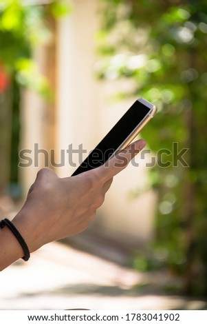 The girl uses the phone, holding it in one hand. Close-up photo. The background contains blurred trees on a bright Sunny day