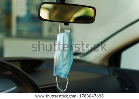 Medical protective face mask in car on the rearview mirror in day - Covid-19 pandemic protection on rear view in the vehicle - coronavirus epidemic new normal prevention concept Royalty-Free Stock Photo #1783047698
