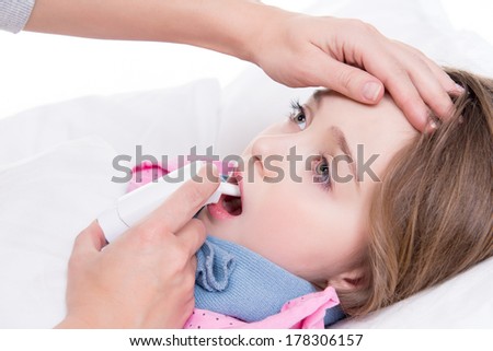 Little girl with sore throat lying in bed and using spray on white background.