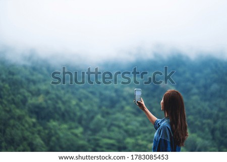 A female tourist using smartphone to take a photo of a beautiful foggy mountains in the forest 